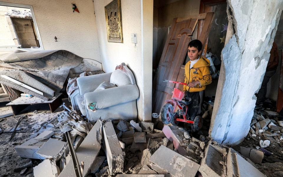 A boy holds a toy plastic tricycle amidst the rubble of a destroyed home in the aftermath of Israeli bombardment on Rafah