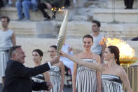 Actress Mary Mina, playing an ancient Greek high priestess, gives the torch with the Olympic Flame to the head of Greece's Olympic Committee, Spyros Capralos, during the Olympic flame handover ceremony at Panathenaic stadium, where the first modern games were held in 1896, in Athens, Friday, April 26, 2024. On Saturday the flame will board the Belem, a French three-masted sailing ship, built in 1896, to be transported to France. (AP Photo/Petros Giannakouris)