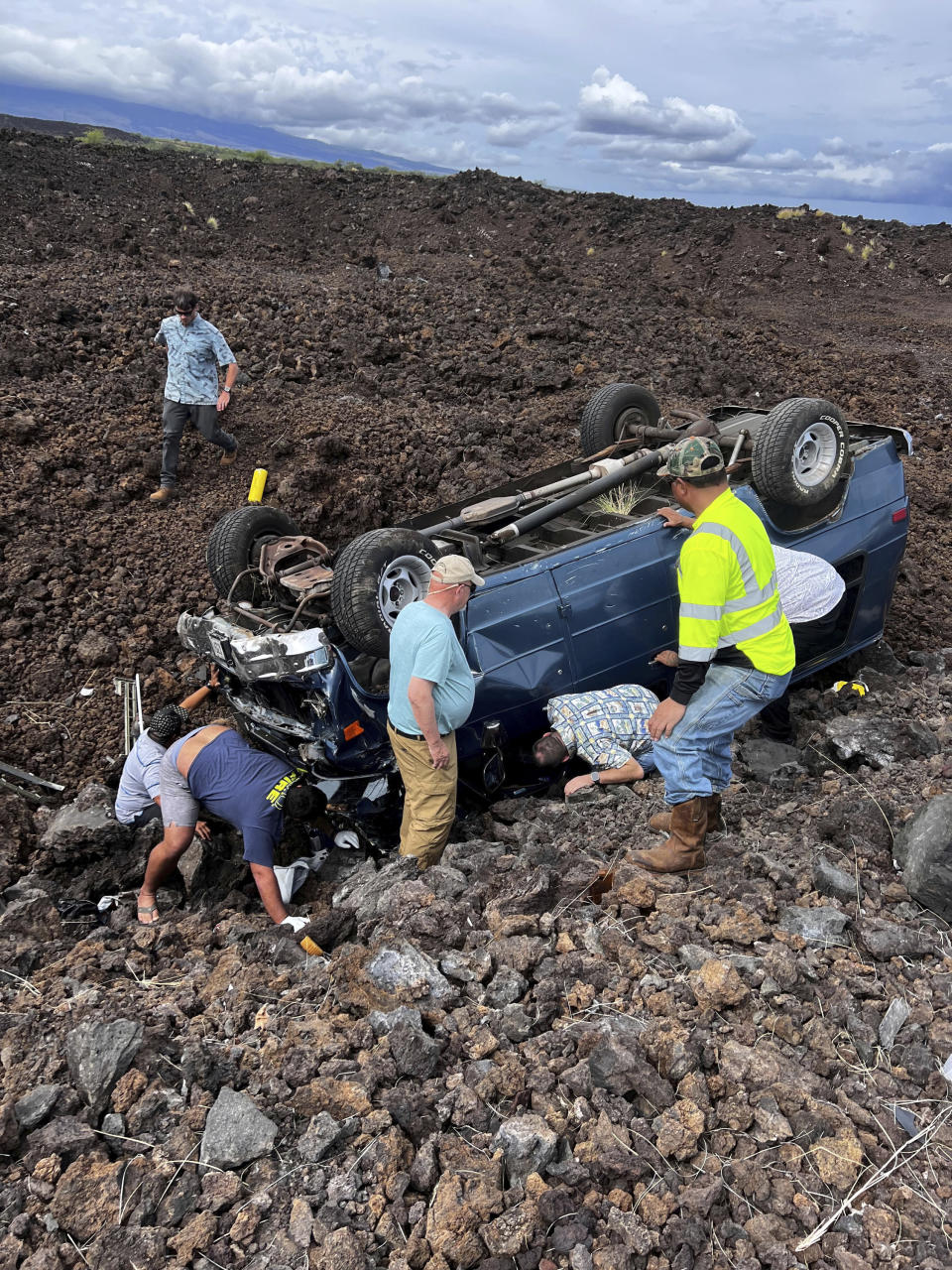 Hawaii Gov. Josh Green, middle, kneels down to look under an upside down vehicle's driver at the scene of an accident in Waikoloa, Hawaii on Thursday, May 18, 2023. Gov. Green, who has worked as an emergency room doctor in rural parts of the Big Island stopped to help out when his security detail spotted a vehicle upside down in a lava field Thursday while en route to a Big Island event. The man suffered a few cuts and bruises and seemed to be OK, Green said. (Reece Kainoa Kilbey/Office of the Governor, State of Hawai'i via AP)