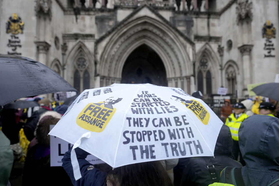 Protesters stand with umbrellas at the Royal Courts of Justice entrance in London, Wednesday, Feb. 21, 2024. Julian Assange's lawyers are on their final U.K. legal challenge to stop the WikiLeaks founder from being sent to the United States to face spying charges. The 52-year-old has been fighting extradition for more than a decade, including seven years in self-exile in the Ecuadorian Embassy in London and the last five years in a high-security prison. (AP Photo/Alastair Grant)