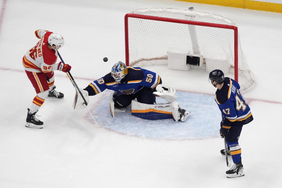 Calgary Flames' Andrei Kuzmenko (96) scores past St. Louis Blues goaltender Jordan Binnington (50) and Torey Krug (47) during the second period of an NHL hockey game Thursday, March 28, 2024, in St. Louis. (AP Photo/Jeff Roberson)