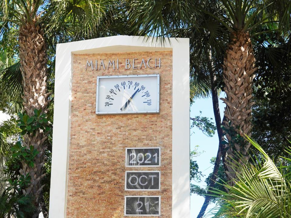 Miami Beach date and temperature on a sign surrounded by palm trees