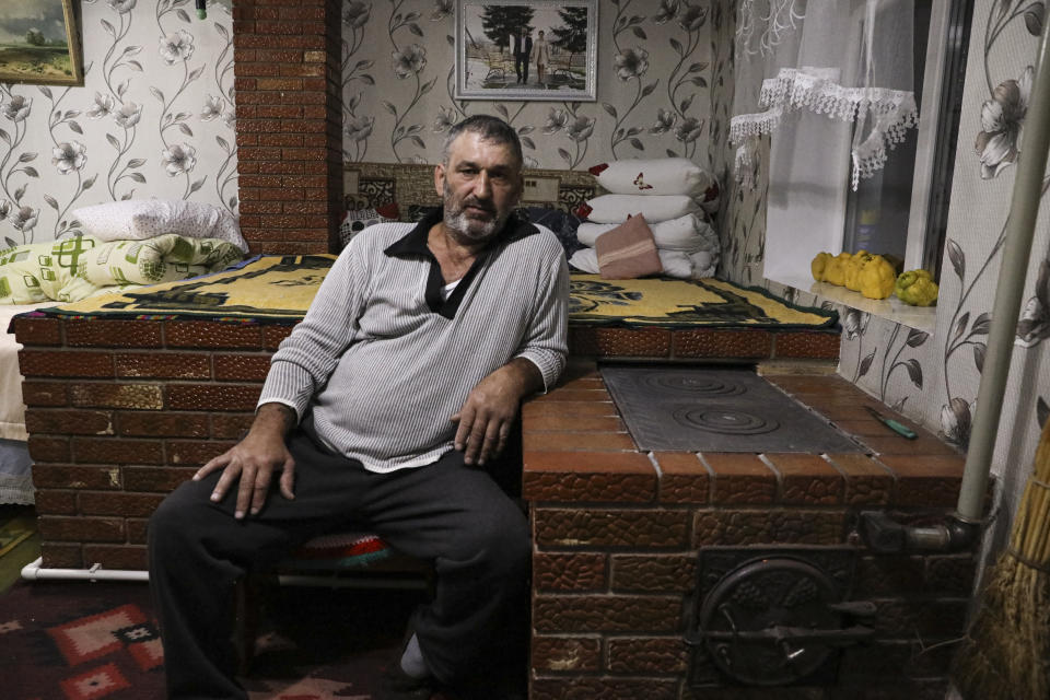 Gheorghe Batca leans on a stove that heats his home outside Chisinau, Moldova, Sunday, Oct. 16, 2022. Europe's energy crisis, triggered by Russia slashing natural gas flows amid its war against Ukraine, has forced some people to turn to cheaper heating sources like firewood as the weather gets colder. But as more people stock up and burn wood, prices have skyrocketed, shortages and thefts have been reported, and scams are emerging. (AP Photo/Aurel Obreja)