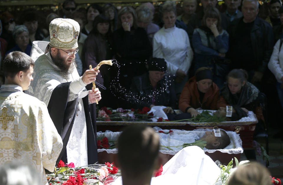 An Orthodox priest sprinkles water during a religious ceremony in front of the coffins of four people killed during last week's operation, in the center of Slovyansk, eastern Ukraine, Wednesday, May 7, 2014. The U.S. and European nations have increased diplomatic efforts ahead of Ukraine's May 25 presidential election, as a pro-Russian insurgency continues to rock the country's eastern regions. (AP Photo/Darko Vojinovic)