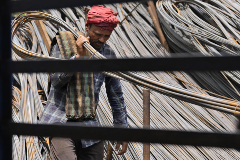 A daily wage laborer carries heavy metal rods to load onto a mini truck on May Day in Prayagraj, India, Monday, May 1, 2023. (AP Photo/Rajesh Kumar Singh)