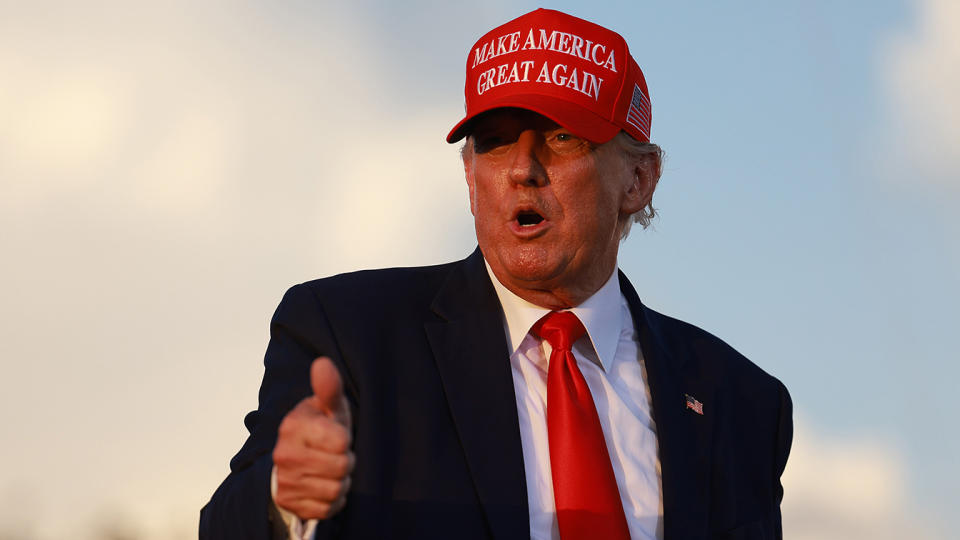 Trump, wearing a Make America Great Again cap, gives a thumbs-up.