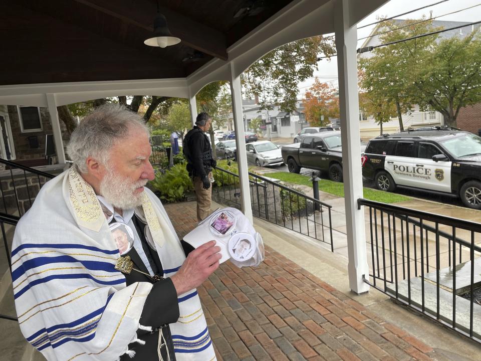 L Edward Mackouse, 80, a worshipper at the Shul at Newtown shows buttons of politicians that he favors at the entrance of the synagogue guarded by a police officer in riot gear in on Saturday, Oct. 14, 2023 in Newtown, Pa. Jews in communities far from Israel gathered at synagogues this weekend for their first Shabbat services as the Israel-Hamas war rages. (AP Photo/Luis Andres Henao)