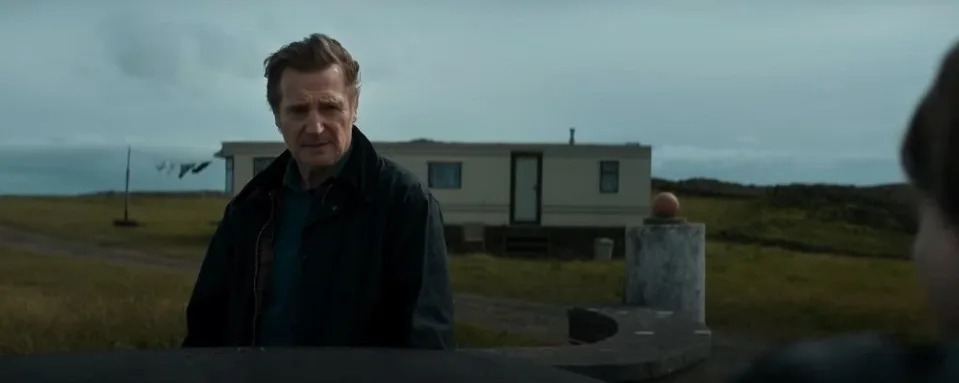 liam neeson in the land of saints and sinners movie, his character stands in front of a caravan and looks concerned