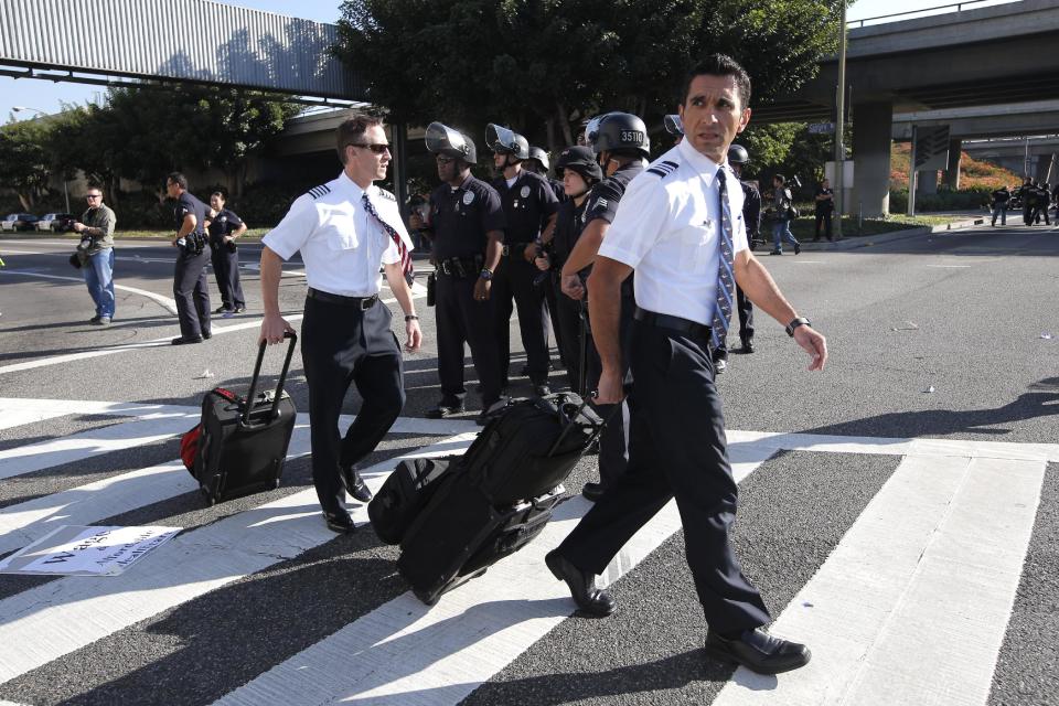 Two flight crew members walk past Los Angeles police officers as union workers at Los Angeles International Airport march along the street in Los Angeles, Wednesday, Nov. 21, 2012. Hundreds of union members marched Wednesday near the entrance to Los Angeles International Airport, where Thanksgiving travelers were warned to arrive early in case of traffic snarls. (AP Photo/Jae C. Hong)