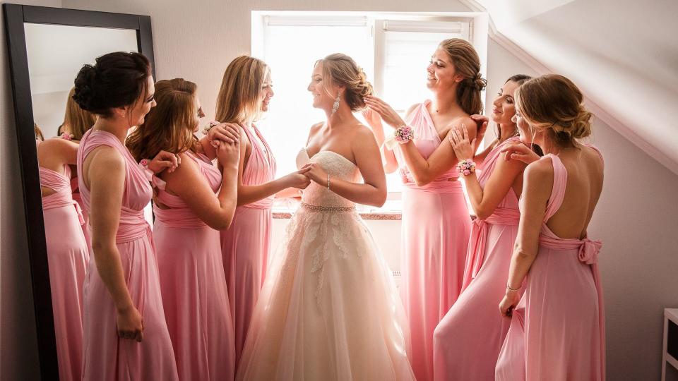 Bride with bridesmaids posing in hotel or fitting room at wedding day.
