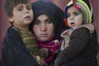 An Afghan woman holds her children as she waits for a consultation outside a makeshift clinic at a sprawling settlement of mud brick huts housing those displaced by war and drought near Herat, Afghanistan, Dec. 16, 2021. The aid-dependent country’s economy was already teetering when the Taliban seized power in mid-August amid a chaotic withdrawal of U.S. and NATO troops. The consequences have been devastating for a country battered by four decades of war, a punishing drought and the coronavirus pandemic. (AP Photo/Mstyslav Chernov)
