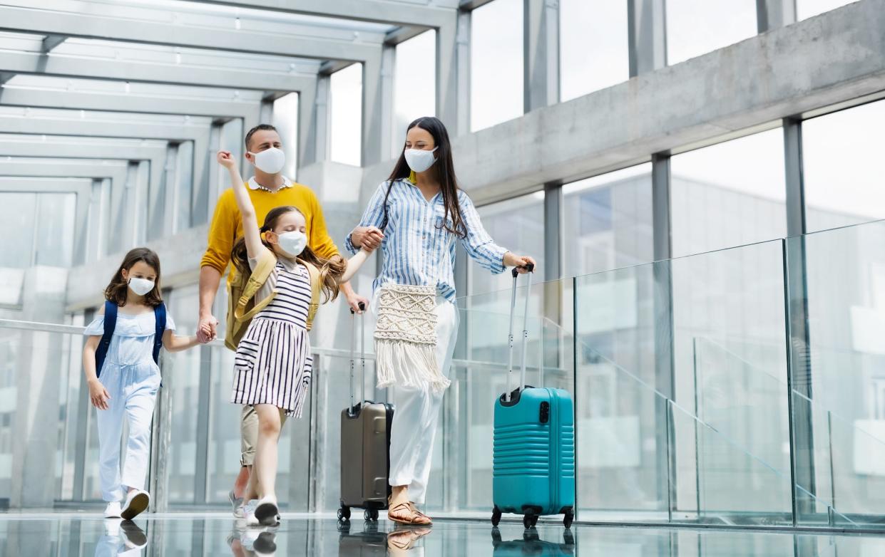 Happy family with two children going on holiday, wearing face masks at the airport.