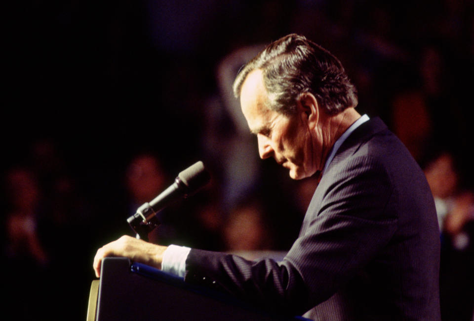 President George H.W. Bush, in profile, stands at a podium