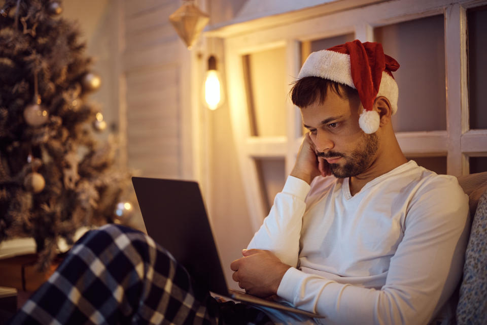 Young man surfing the net on laptop while feeling bored on Christmas Eve at home.