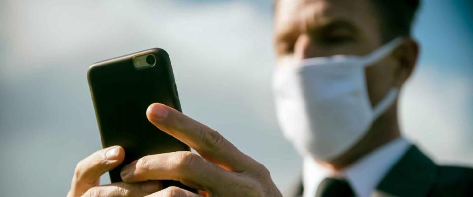 Worried businessman wearing surgical face mask checking his smartphone for coronavirus news updates outdoors