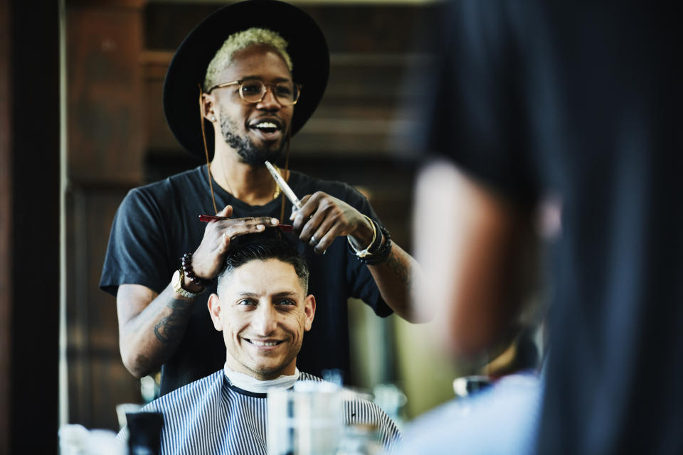 A hairstylist or barber cuts a man's hair in front of a mirror