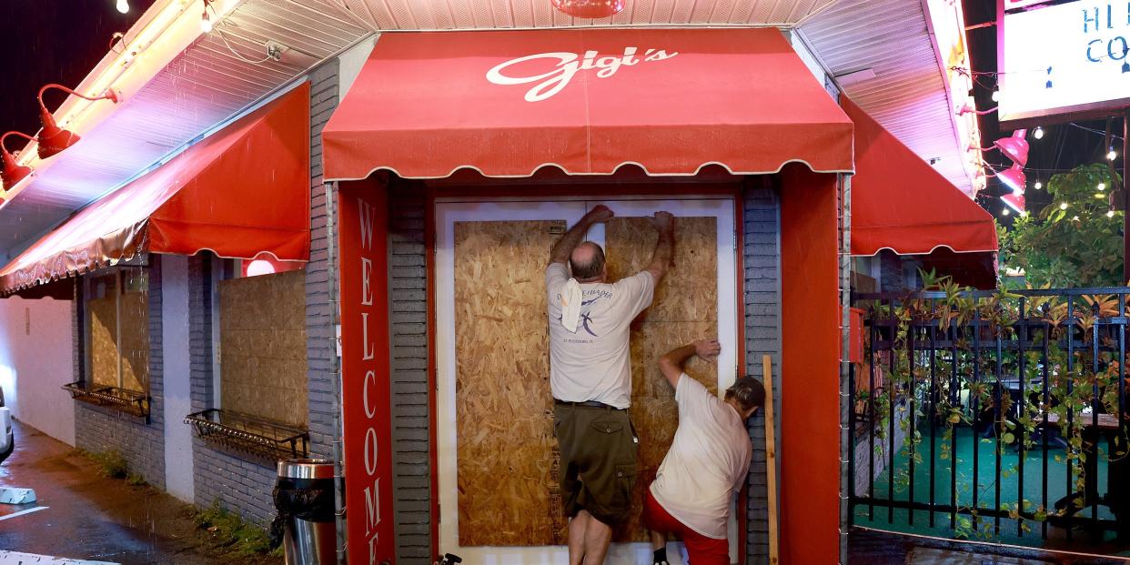 Two people boarding up storefront with wood in Florida.