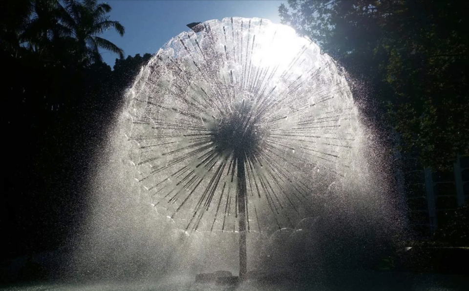 Water spraying from a spherical dandelion-shaped fountain backlit by sunlight
