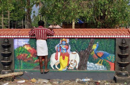 A man looks out from a boundary wall with an image of a Hindu deity in the compound of Puttingal Devi temple where a fire broke out on Sunday, in Kollam in the southern state of Kerala, India, April 11, 2016. REUTERS/Sivaram V
