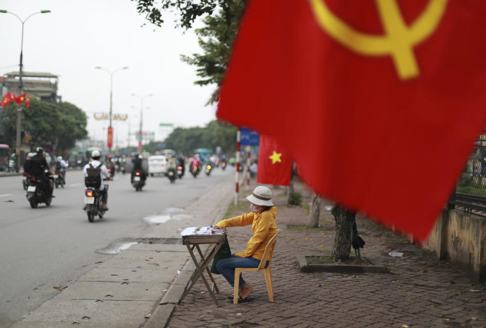 A lottery vender waits for customers under a national flag in Hanoi, Vietnam on Thursday, Aug. 6, 2020. Vietnamese health official said on Thursday the COVID-19 outbreak would peak in the coming ten days as the country reported another death and a score of new infections. (AP Photo/Hau Dinh)