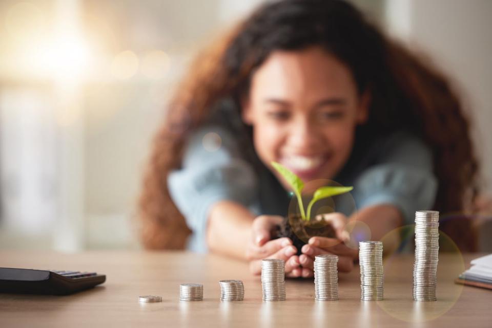 A person holds a seedling in the background with increasingly taller stacks of coins in the foreground. 