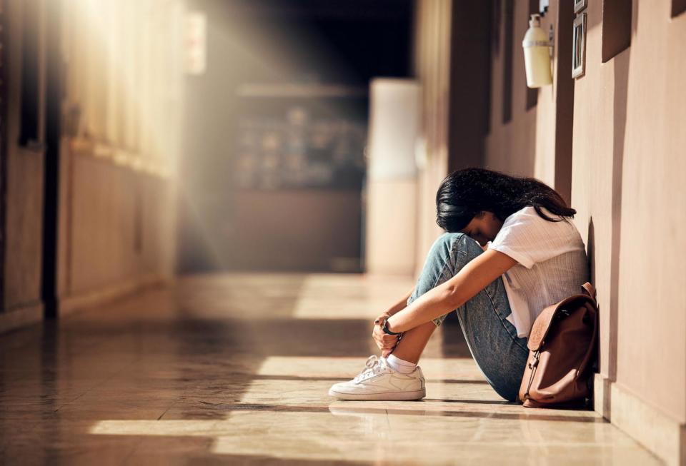 PHOTO: A depressed girl at university sits on the flood of the hallway. (Adobe Stock)