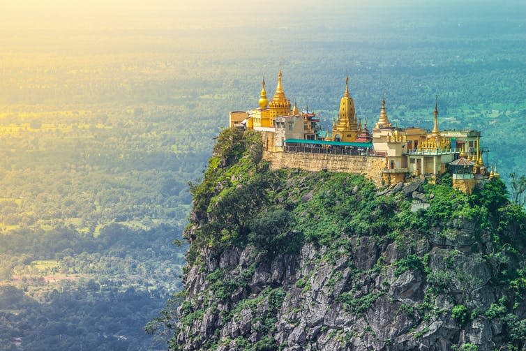 Golden buildings on top of a steep rocky summit.