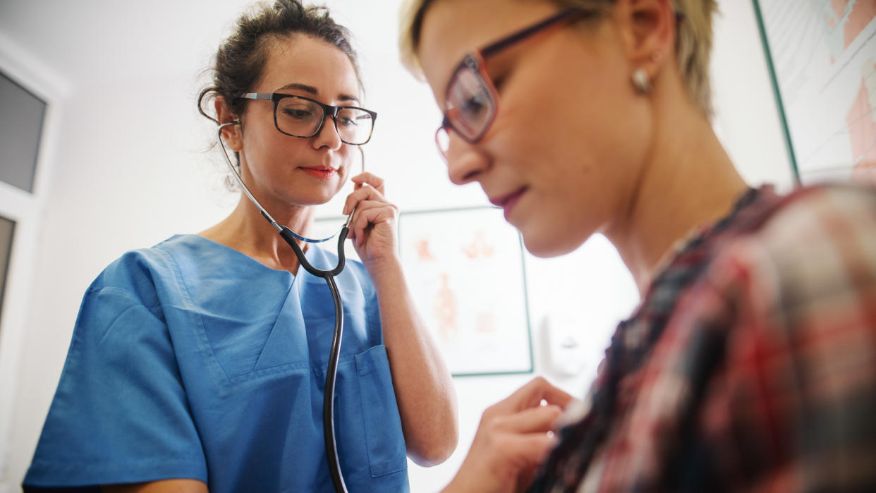 Female middle-aged doctor using stethoscope to examine patient.