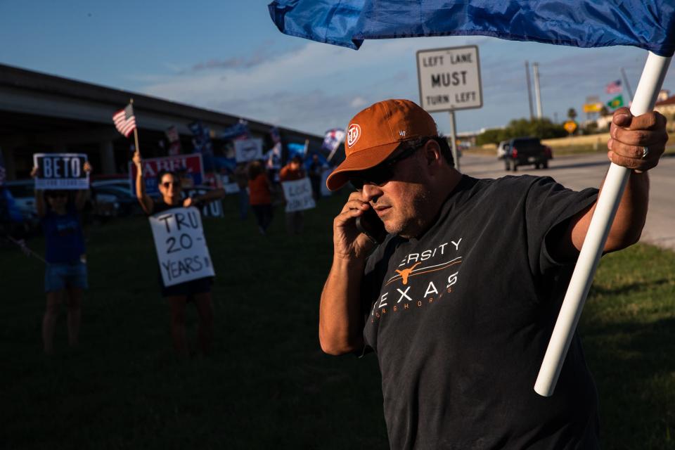Nueces County Democratic Party Chair Rene Saenz calls in to a local radio station to give a comment while holding a flag in support of President Joe Biden at the intersection of Terry Shamsie Boulevard and Highway 77 in Robstown, Texas, on Saturday, Oct. 22, 2022. The protest was organized by Saenz to counter former President Donald Trump's rally nearby at the regional fairgrounds.