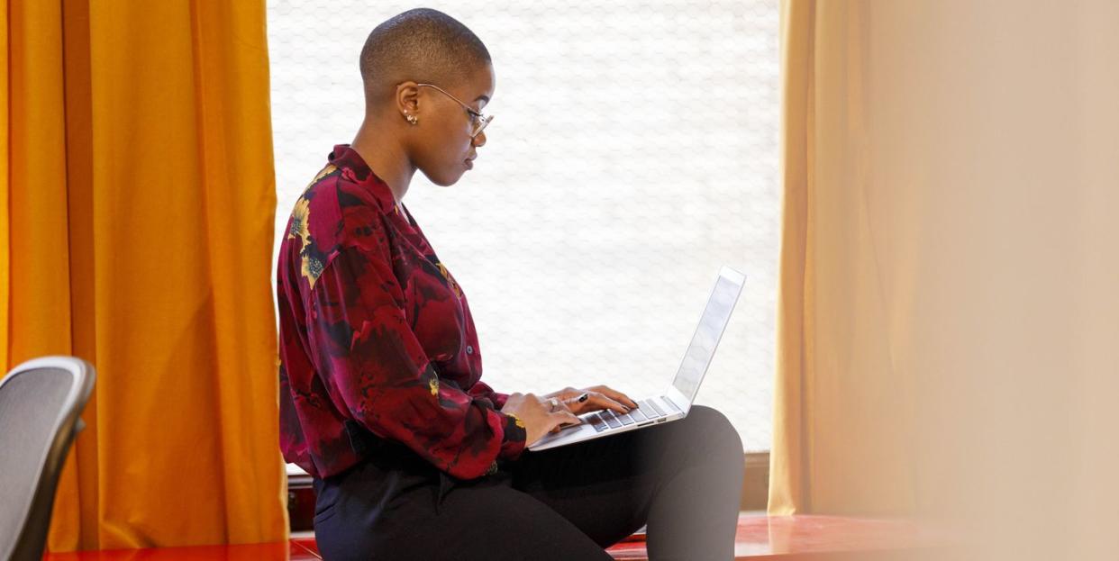 side view of woman working on laptop near window