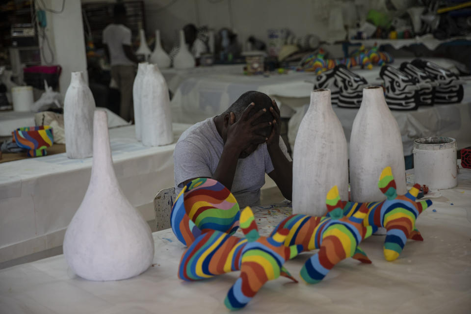 Un trabajador se toma un descanso mientras monta piezas de arte en Caribbean Craft, una empresa propiedad de Magalie Dresse, en Puerto Príncipe, Haití, el 14 de septiembre de 2021. La empresa de Dresse envía unos 50 contenedores de arte haitiano a Estados Unidos cada año. Pero antes de llegar al puerto, deben pasar por zonas controladas por las pandillas. (AP Foto/Rodrigo Abd)