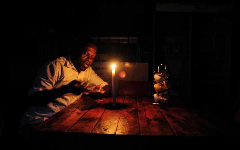 A restaurant owner counts South African rand banknotes by candlelight during a loadshedding power outage period, in Johannesburg, South Africa - Leon Sadiki/Bloomberg