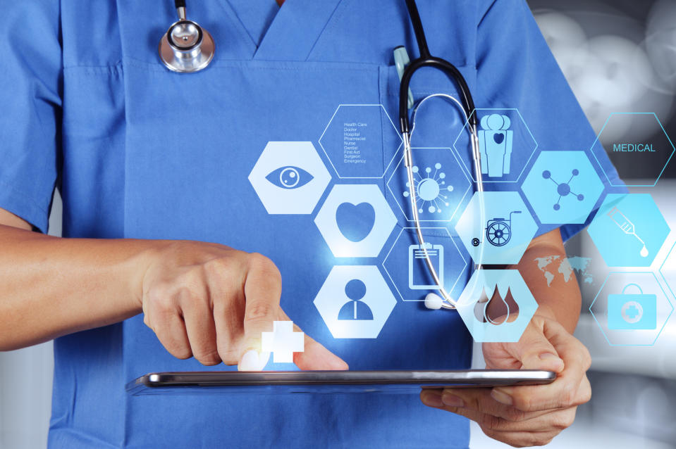 Doctor holding a tablet with healthcare icons appearing above the tablet