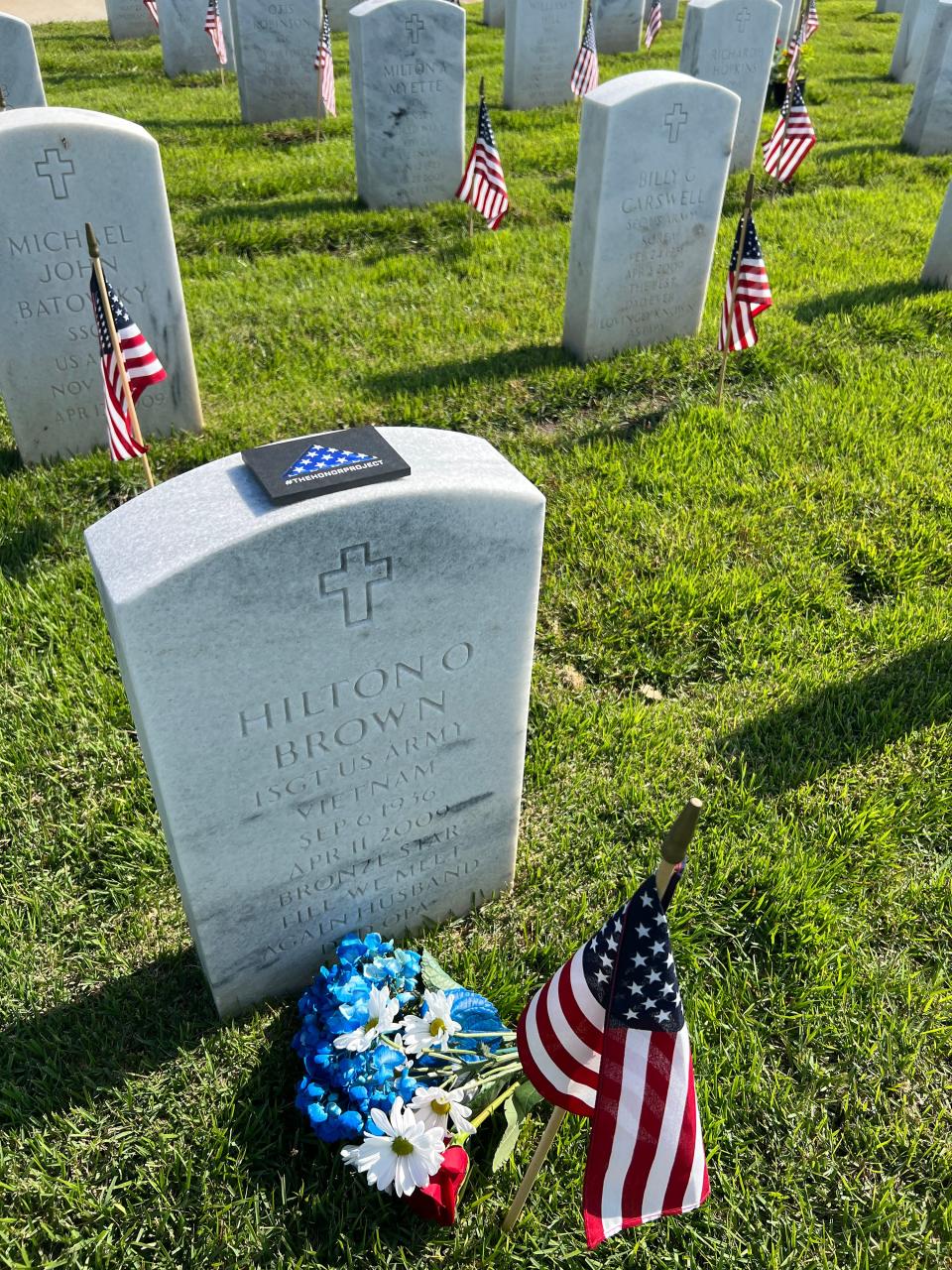 A hand-crafted "Flags of Valor" commemorative token is shown on a grave stone at the Jacksonville Memorial Cemetery. The tokens were placed by volunteers for the Travis Manion Foundation and Wounded Warrior Project.