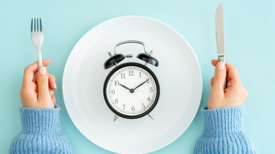 A white dish with a clock set on a blue background, with a woman holding a fork and knife