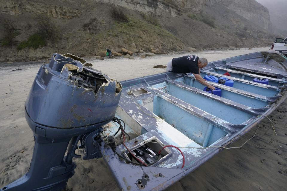 Boat salvager Robert Butler picks up a canister in one of one of two boats sitting on Blacks Beach, Sunday, March 12, 2023, in San Diego. Authorities say multiple people were killed when two suspected smuggling boats overturned off the coast in San Diego, and crews were searching for additional victims. (AP Photo/Gregory Bull)