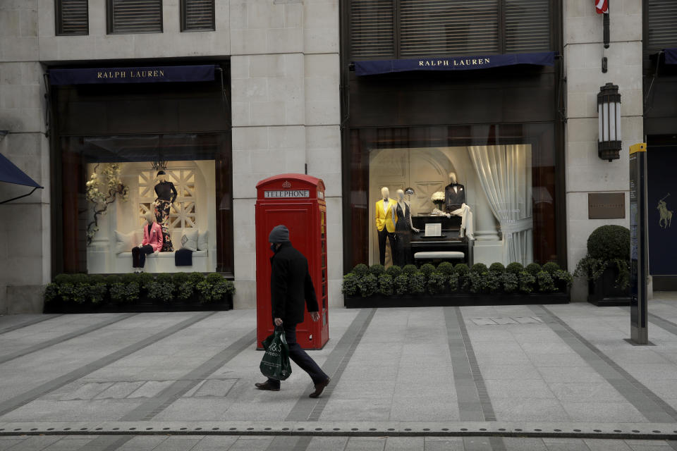 A person wearing a mask to curb the spread of coronavirus walks a traditional red phone box outside the Ralph Lauren fashion brand flagship store on New Oxford Street in London, during England's third coronavirus lockdown, Friday, March 26, 2021. The pandemic has battered the British economy, which has suffered its deepest recession in more than 300 years. Pubs, restaurants, theaters, hair salons and all stores selling nonessential items such as books and footwear have spent much of the past year closed. (AP Photo/Matt Dunham)