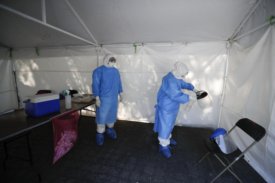 A healthcare worker disinfects a workspace at the end of a day of collecting sample to test for the new coronavirus inside a mobile diagnostic tent, in the Coyoacan district of Mexico City, Friday, Nov. 13, 2020. Mexico City announced Friday it will order bars closed for two weeks after the number of people hospitalized for COVID-19 rose to levels not seen since August. (AP Photo/Eduardo Verdugo)