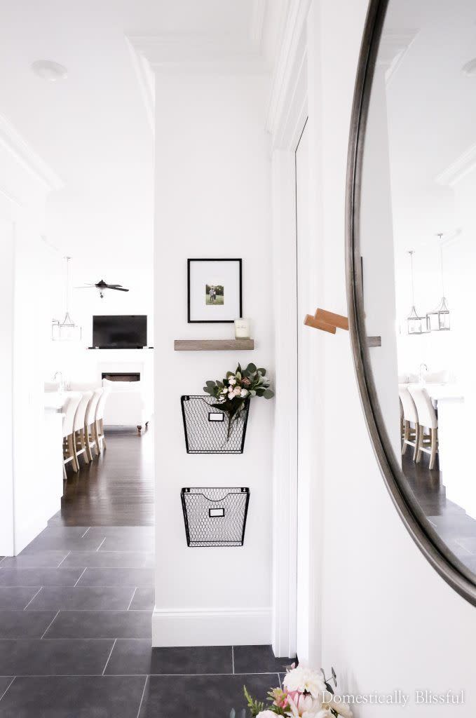 a white hallway with a mirror and wire baskets on wall