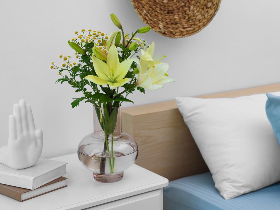 yellow flowers in a clear vase on nightstand beside wooden bed with blue sheets