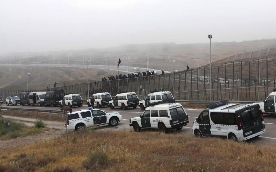 Spanish Guardia Civil officers cordon off the area as sub-Saharan migrants sit on top of a metallic fence that divides Morocco and the Spanish enclave of Melilla, Thursday, May 1, 2014. Spain says around 700 African migrants have rushed its barbed wire border fences in the North African enclave of Melilla, and although police repelled most, 140 managed to enter Spanish territory. The migrants charged the fences in two waves, with 500 arriving in the early hours and another 200 later Thursday morning. Spain and Morocco stepped up border vigilance in Feb. when 15 migrants drowned trying to enter Spain's other north African coastal enclave, Ceuta. (AP Photo/Fernando Garcia)