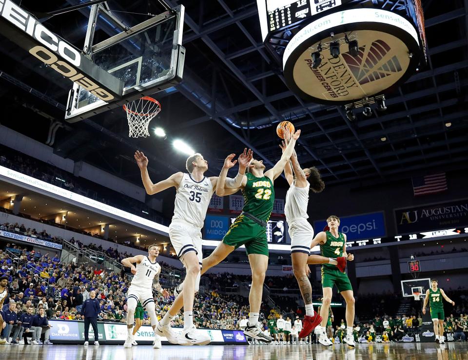 Kareem Thompson #2 of the Oral Roberts Golden Eagles leaps for a rebound amidst pressure from Joshua Streit #22 of the North Dakota State Bison at the 2023 Summit League Basketball Championship at the Denny Sanford Premier Center in Sioux Falls, South Dakota.
