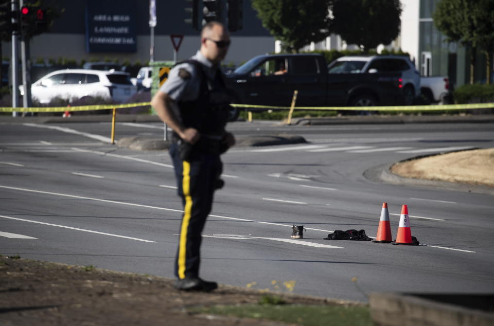 An RCMP officer stands near a shoe with blood on it and other belongings on the road at the scene of a shooting in Langley, British Columbia, Monday, July 25, 2022. Canadian police reported multiple shootings of homeless people Monday in a Vancouver suburb and said a suspect was in custody. (Darryl Dyck/The Canadian Press via AP)