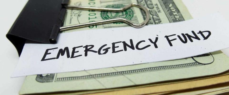 Closeup of US dollars in paper clip on white background with note written EMERGENCY FUND : Concept of setting money saving goal for rainy day.