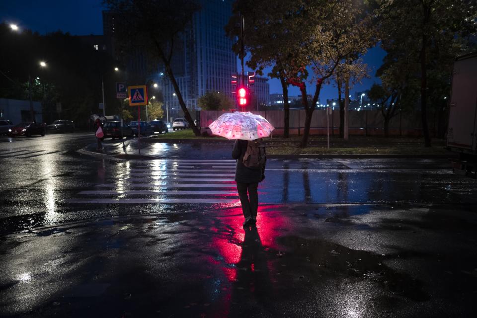 A pedestrian holds an umbrella as he waits for a green traffic light on an almost empty street during an autumn rain in Moscow, Russia, Tuesday, Sept. 21, 2021. The temperature in Moscow dropped to about 7 degrees (44,6 degrees Fahrenheit). (AP Photo/Alexander Zemlianichenko)