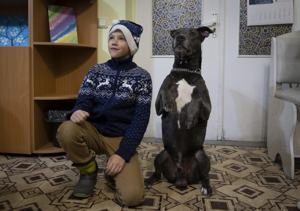 A boy poses for photo with an American Pit Bull Terrier "Bice" in the Center for Social and Psychological Rehabilitation in Boyarka close Kyiv, Ukraine, Wednesday, Dec. 7, 2022. Bice is an American pit bull terrier with an important and sensitive job in Ukraine — comforting children traumatized by the war. The Center for Social and Psychological Rehabilitation is a state-operated community center where a group of people are trying to help those who have experienced a trauma after the Feb. 24 Russian invasion, and now they are using dogs like Bice to give comfort. (AP Photo/Vasilisa Stepanenko)