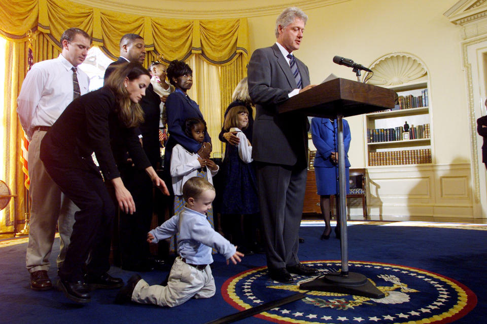 UNITED STATES - NOVEMBER 30:  Katie Banks reaches for her son, Collin, who's not paying much attention to President Bill Clinton in the Oval Office. Collin's father, Eric (left), and members of other families look on as Clinton announces an order allowing states to develop paid-leave programs for parents who have newborns or recently adopted children.  (Photo by Harry Hamburg/NY Daily News Archive via Getty Images)