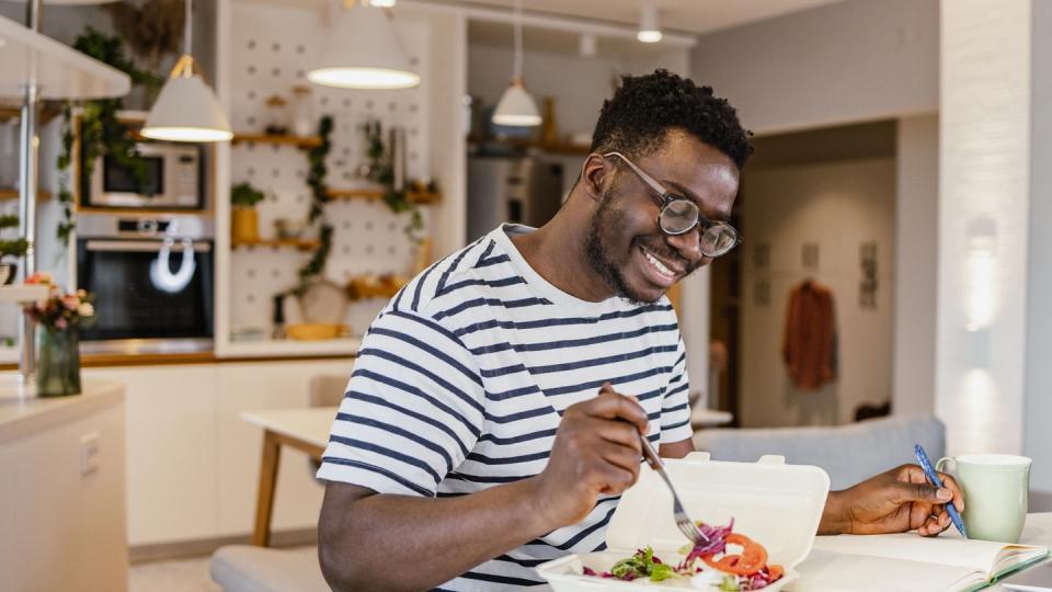 young african american man eating takeaway meal at home and planning activities