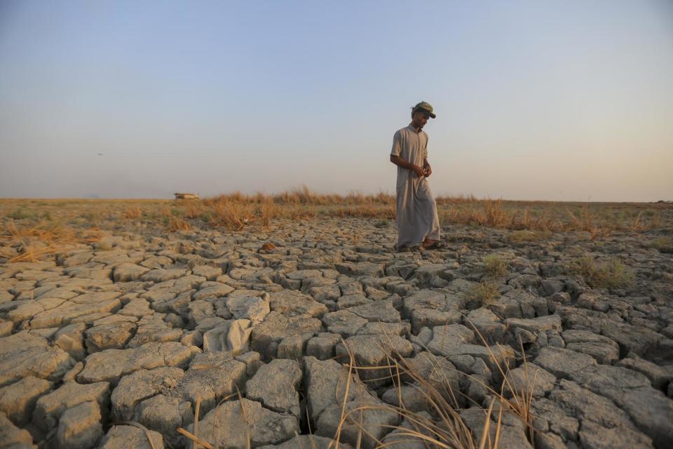 A man walks over dry, cracked earth.