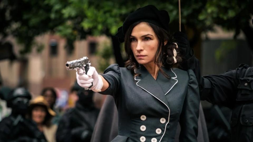 A woman dressed in formal black clothes and white gloves aims a gun